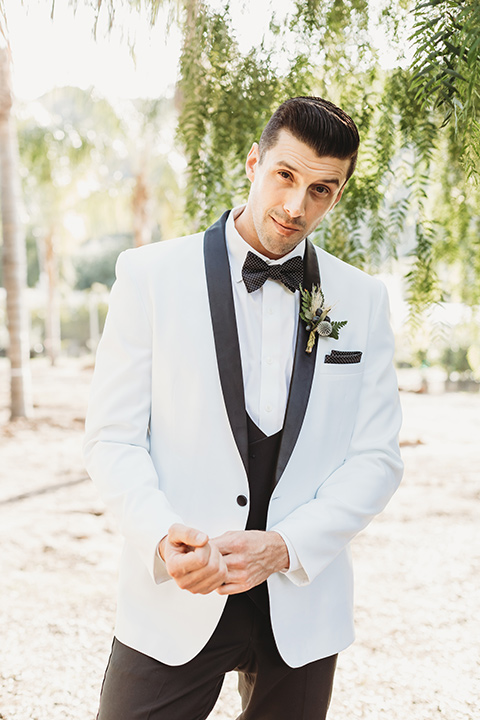  groom in a white tuxedo with a black shawl lapel detail and a black and white polka dot bow tie