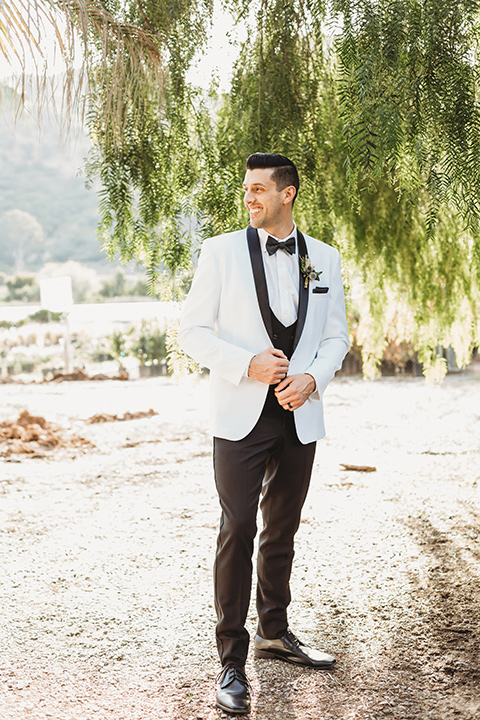  groom in a white tuxedo with a black shawl lapel and a black and white polka dot bow tie