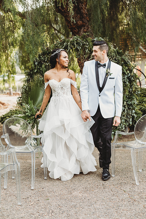  bridal hair with a braid and headpiece in a lace ballgown with an off the shoulder detail and the groom in a white with black shawl lapel tuxedo – bride walking down the aisle