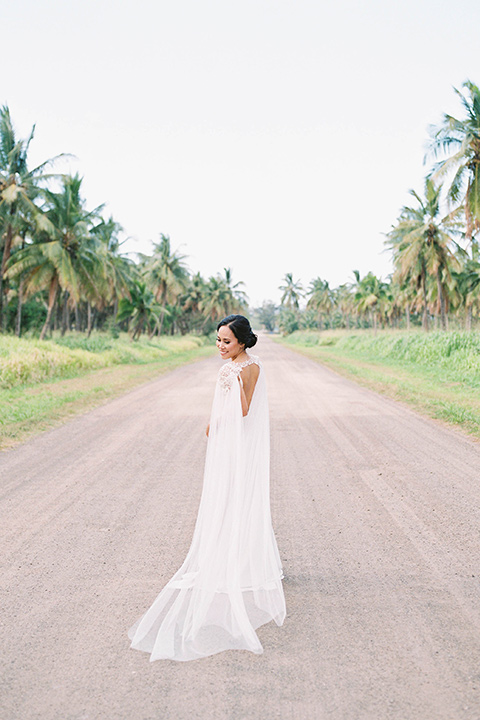  bride in a white formfitting gown with a long ethereal cape and her hair in a low bun 