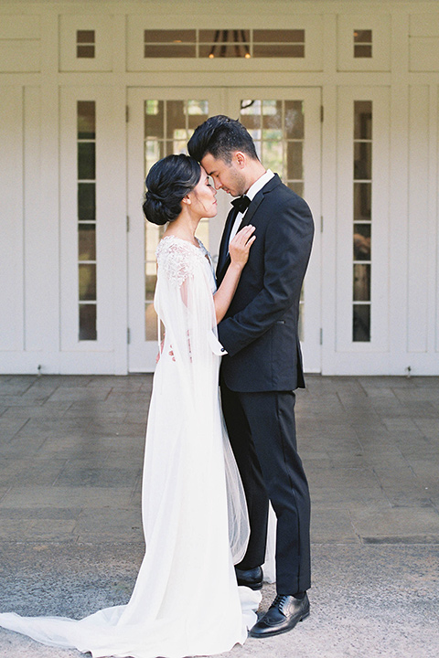  and the groom in a black notch lapel tuxedo with bow tie outside of venue