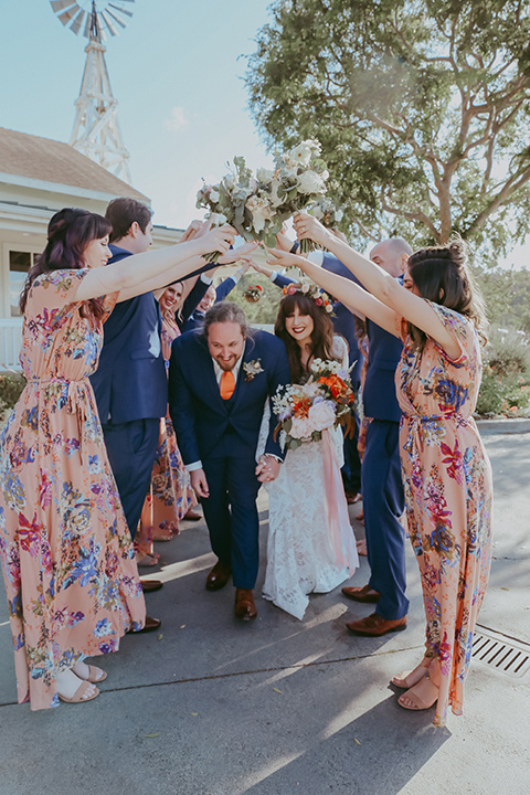  bride in a lace bohemian gown with tulip sleeves and a braided crown, the groom in a cobalt blue suit for purchase and the groomsmen in rental cobalt suits and the bridesmaids in pink floral gowns 