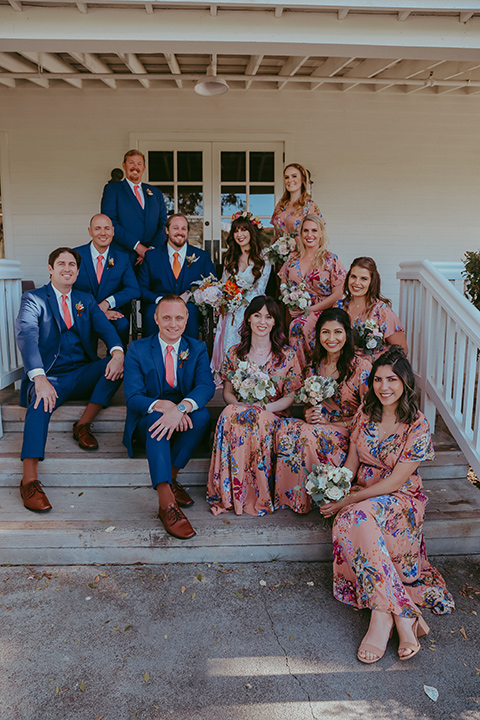  bride in a lace bohemian gown with tulip sleeves and a braided crown, the groom in a cobalt blue suit for purchase and the groomsmen in rental cobalt suits and the bridesmaids in pink floral gowns 