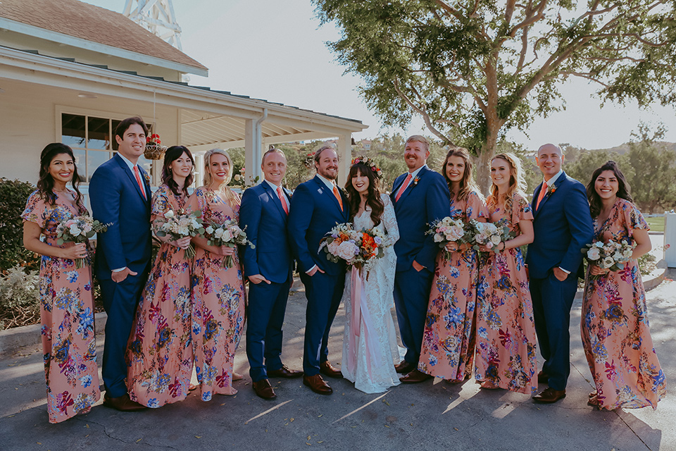  bride in a lace bohemian gown with tulip sleeves and a braided crown, the groom in a cobalt blue suit for purchase and the groomsmen in rental cobalt suits and the bridesmaids in pink floral gowns 