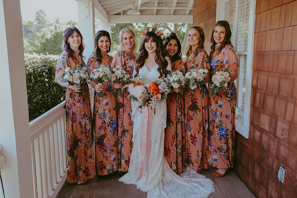  bride in a lace bohemian gown with tulip sleeves and a braided crown, and the bridesmaids in pink floral gowns 