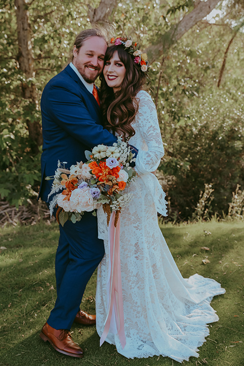  bride in a lace bohemian gown with tulip sleeves and a braided crown, the groom in a cobalt blue suit for purchase with a burnt orange tie 