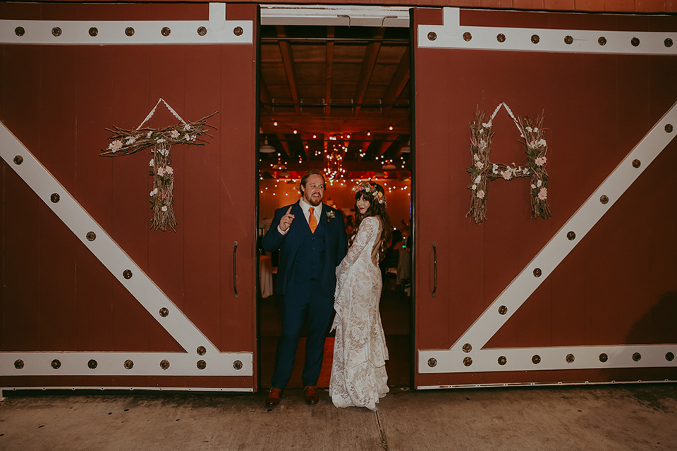  bride in a lace bohemian gown with tulip sleeves and a braided crown, the groom in a cobalt blue suit for purchase in front of a barn