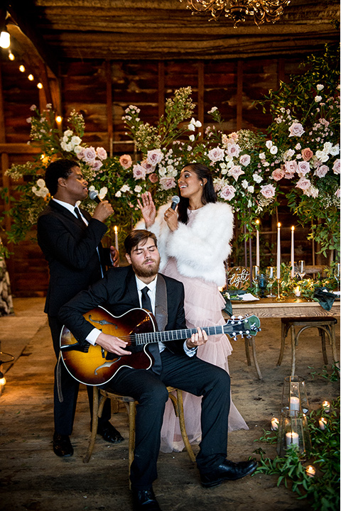  bride in a white ballgown with her hair in a loose brain and garden bouquet the groom in a green suit sitting at the table