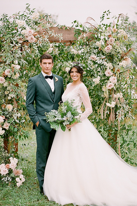  bride in a white ballgown with her hair in a loose brain and garden bouquet the groom in a green suit at ceremony