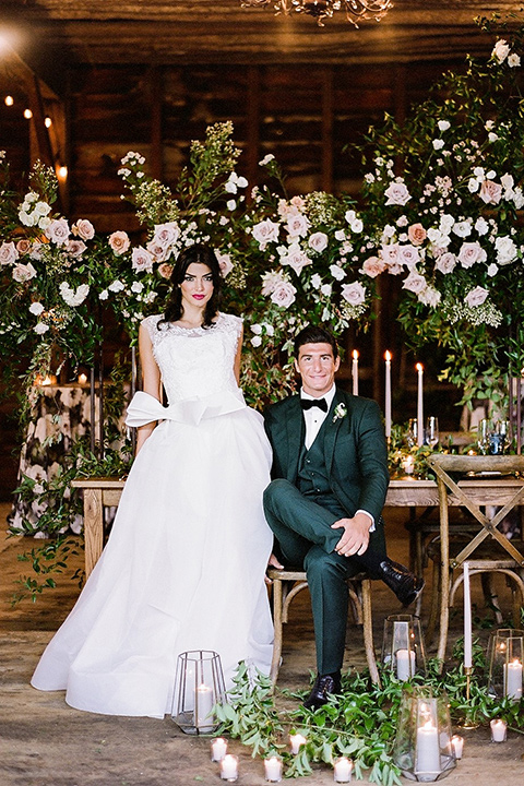  bride in a white ballgown with her hair in a loose brain and garden bouquet the groom in a green suit sitting