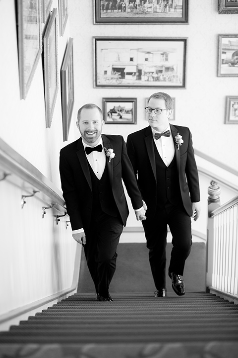 grooms in black tuxedos with white shirts and black bow ties walking up the stairs