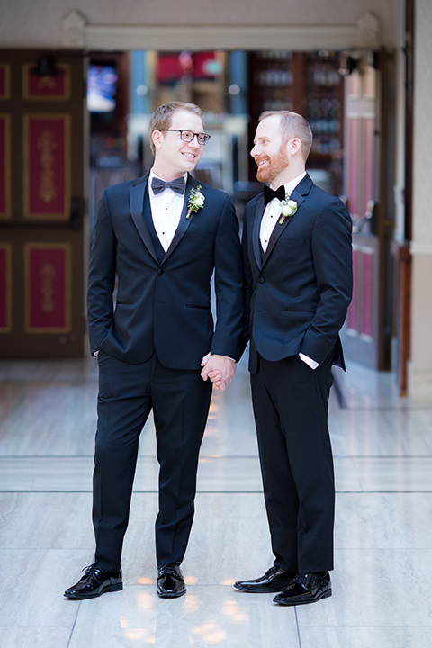  grooms in black tuxedos with white shirts and black bow ties standing outside