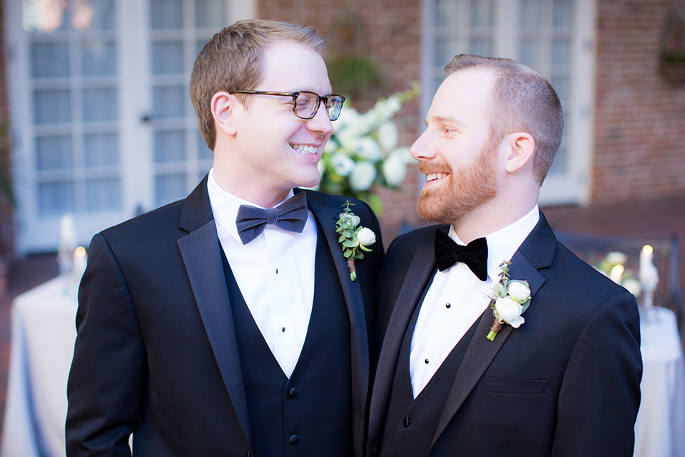 grooms in black tuxedos with white shirts and black bow ties smiling