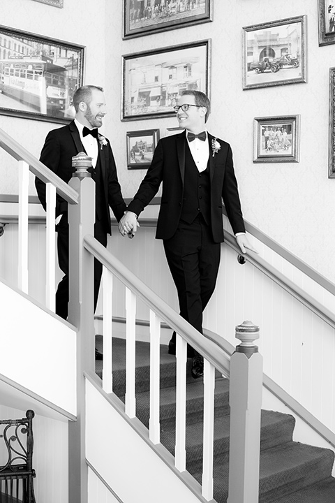  grooms in black tuxedos with white shirts and black bow ties walking down the stairs