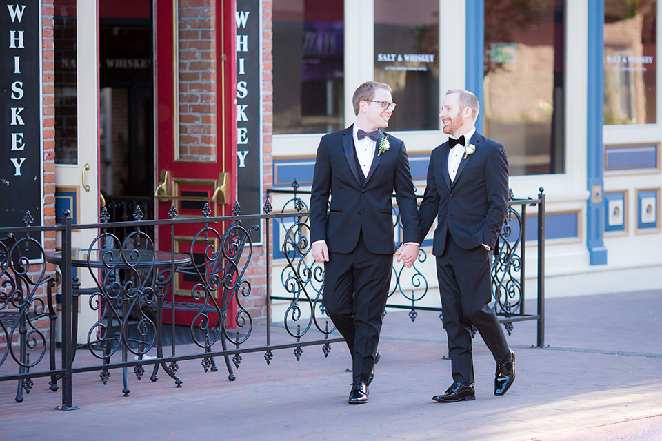 grooms in black tuxedos with white shirts and black bow ties walking outside venue