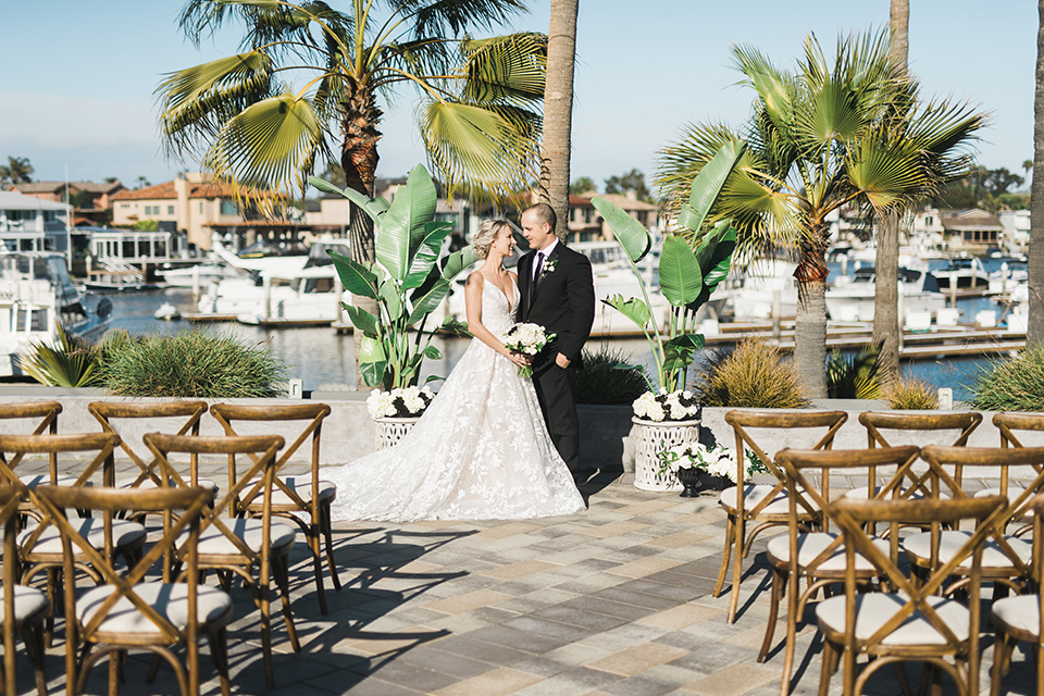 bride in a white flowing gown with deep v neck line and thin straps, the groom is in a black tuxedo at the ceremony space