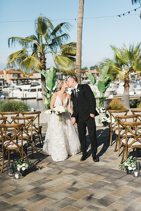 bride in a white gown with a deep v neckline and thin straps and the groom in a black tuxedo kissing at the ceremony