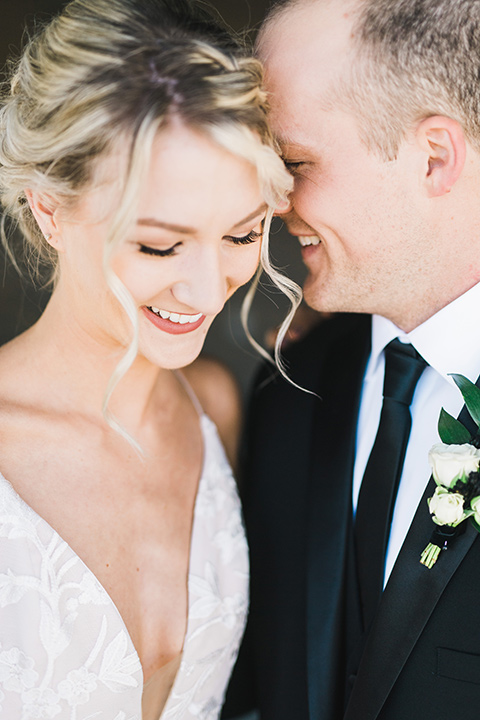 bride in a white flowing gown with thin straps and hair in a lose bun, the groom in a black tuxedo and black long tie close up together