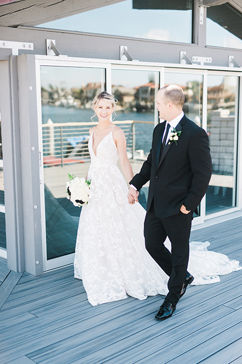 bride in a white flowing gown with thin straps and hair in a lose bun, the groom in a black tuxedo and black long tie- walking together