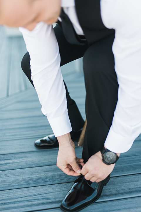 groom in a black tuxedo tying his shoes 