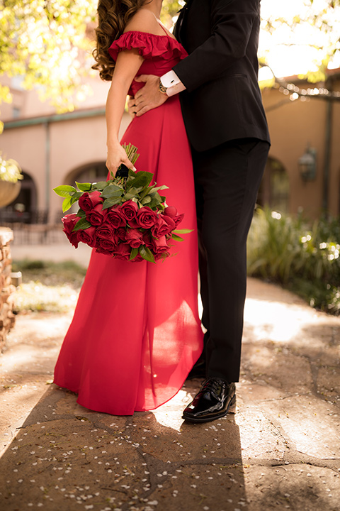 girl in a long red dress with an off the shoulder detail and roses and man in a black tuxedo with a shawl lapel tuxedo and a black bow tie