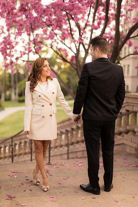 girl in a long white trench coat and man in a black tuxedo with a shawl lapel tuxedo and a black bow tie twirling