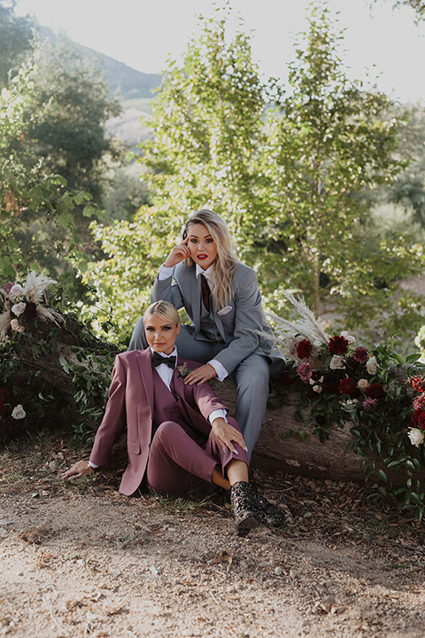  one bride wearing a rose pink suit with a geometric bow tie and the other wearing a light blue suit and a wine burgundy colored bow tie 