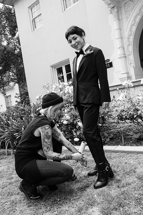 a model in a black tuxedo and a woman helping her look her best 