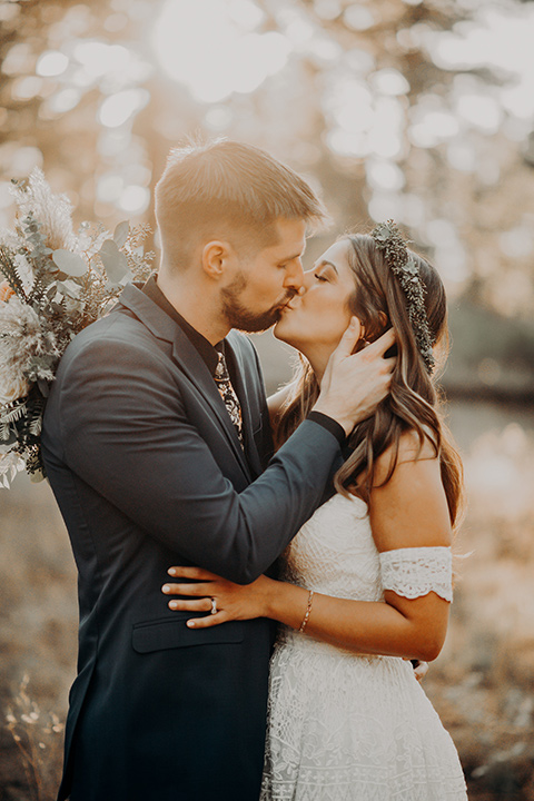  bride in a bohemian gown with an off the shoulder detail and a floral crown and the groom in a blue suit with bow tie 