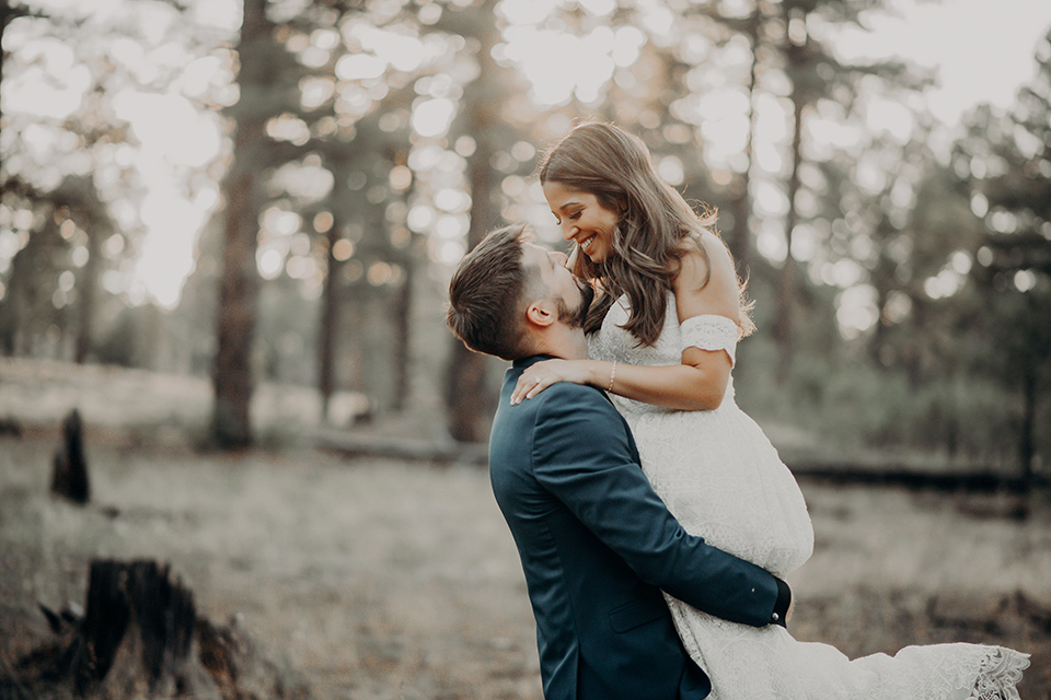  groom in a dark blue suit with a bow tie, the bride in a flowing white gown with an off the shoulder detail 