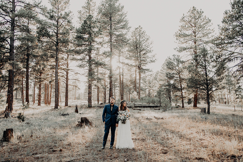  groom in a dark blue suit with a bow tie, the bride in a flowing white gown with an off the shoulder detail 