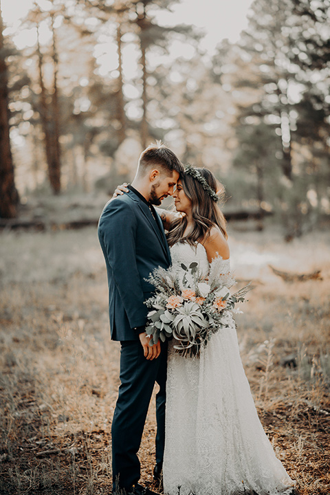  bride in a bohemian gown with an off the shoulder detail and a floral crown and the groom in a blue suit with bow tie