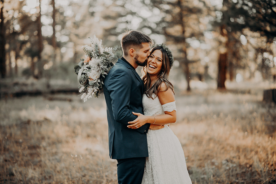  groom in a dark blue suit with a bow tie, the bride in a flowing white gown with an off the shoulder detail 