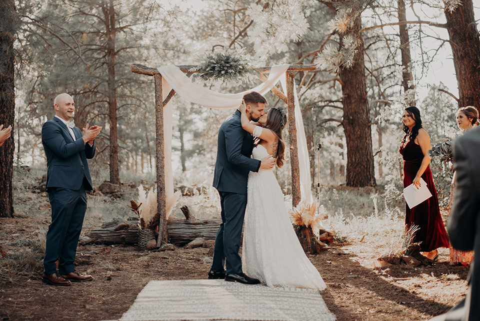  groom and groomsmen in dark blue suits with bow ties, bridesmaids in soft pastel colors in different patterns and designs, the bride in a flowing white gown with an off the shoulder detail 