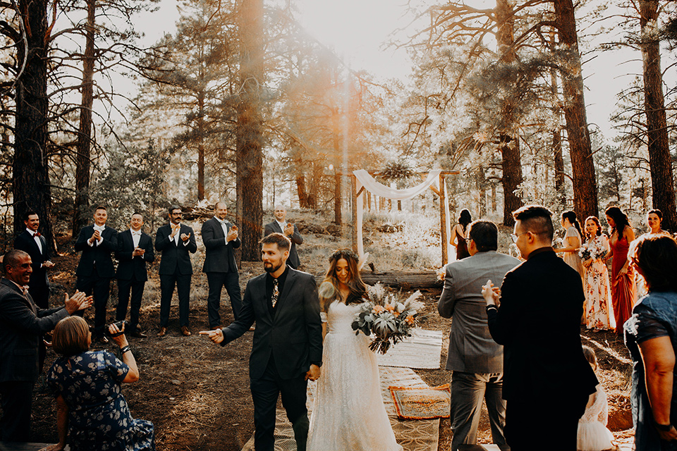  groom and groomsmen in dark blue suits with bow ties, bridesmaids in soft pastel colors in different patterns and designs, the bride in a flowing white gown with an off the shoulder detail 