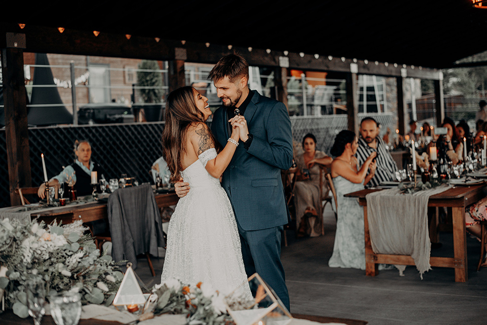  groom and groomsmen in dark blue suits with bow ties, bridesmaids in soft pastel colors in different patterns and designs, the bride in a flowing white gown with an off the shoulder detail 