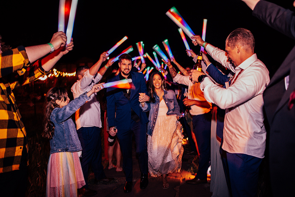  groom and groomsmen in dark blue suits with bow ties, bridesmaids in soft pastel colors in different patterns and designs, the bride in a flowing white gown with an off the shoulder detail 