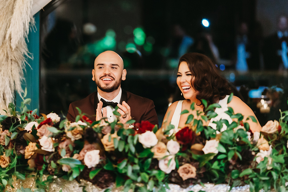  bride in a white ballgown with a plunging neckline and long veil and the groom in a burgundy tuxedo with a black shawl lapel, the bridesmaids in burgundy gowns and the groomsmen in black tuxedos