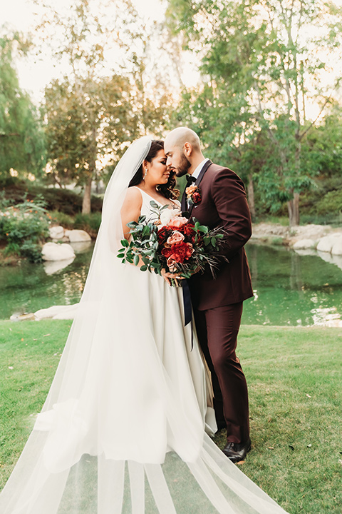  bride in a white ballgown with a plunging neckline and long veil and the groom in a burgundy tuxedo with a black shawl lapel 