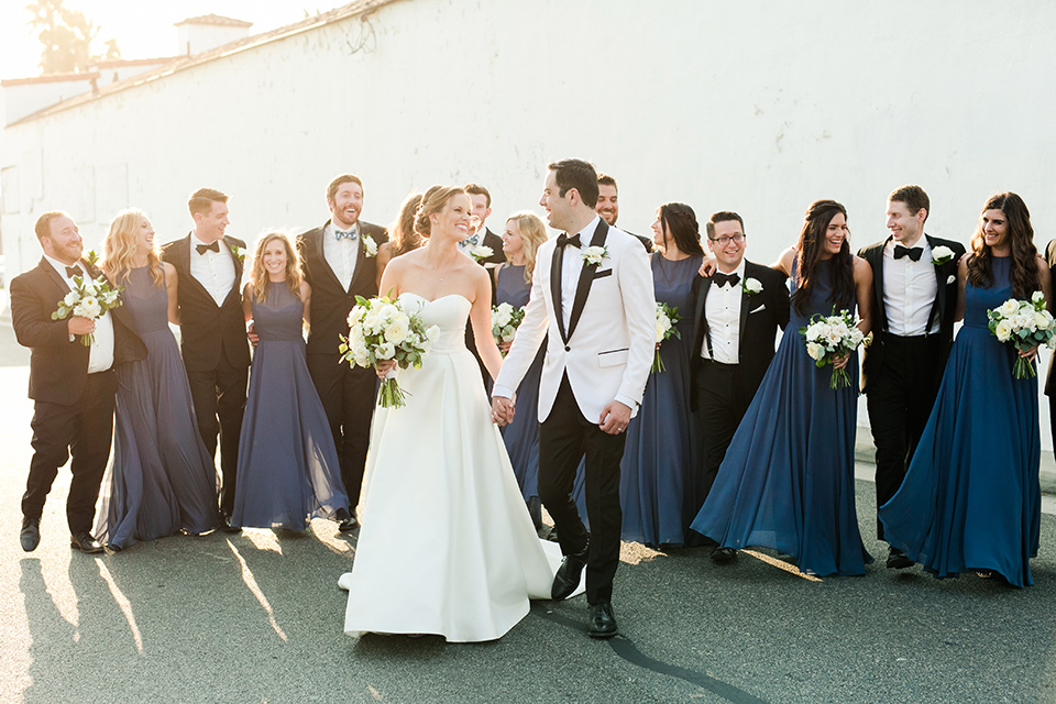  bride in a ballgown with a sweetheart neckline and the groom in a black tuxedo, the bridesmaids wore deep teal blue gowns and the groomsmen in a black tuxedo with blue bow ties 