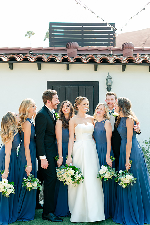  bride in a ballgown with a sweetheart neckline and bridesmaids in deep teal gowns and the bridesman in a black tux with blue bow tie 