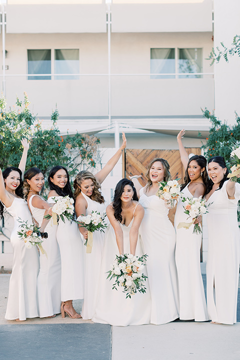  bride in a white modern ballgown with pockets and a low cut neckline and bridesmaids in neutral gowns