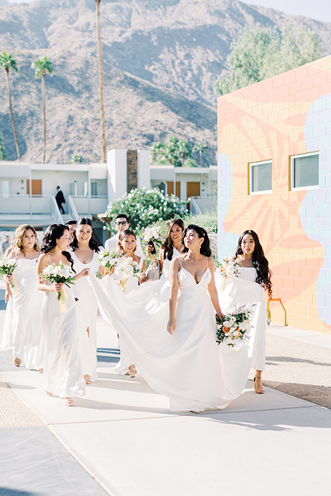  bride in a white modern ballgown with pockets and a low cut neckline and bridesmaids in neutral gowns