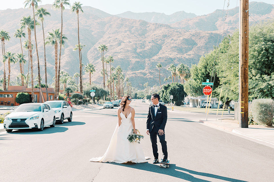  bride in a white modern gown with a low cut neckline and pockets and the groom in a black tuxedo and bow tie, the bridesmaids in neutral colored gowns and groomsmen in black tuxedos at the reception