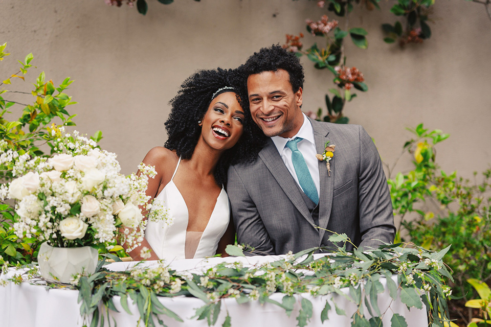  bride in a white lace formfitting gown with a V-neckline, and the groom in a café brown suit a dusty teal long tie 