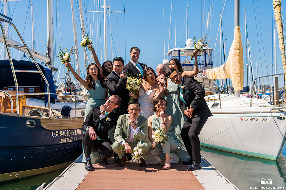  bride in a white lace form fitting gown with a strapless sweetheart neckline, the groom in a black tuxedo with a black bow tie, the groomsmen in black tuxedos with teal bow ties, the the bridesmaids in mint blue gowns and the bridesman in a mint suit to match the girls’ gown