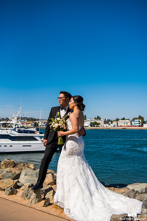  bride in a white lace form fitting gown with a strapless sweetheart neckline, the groom in a black tuxedo with a black bow tie 