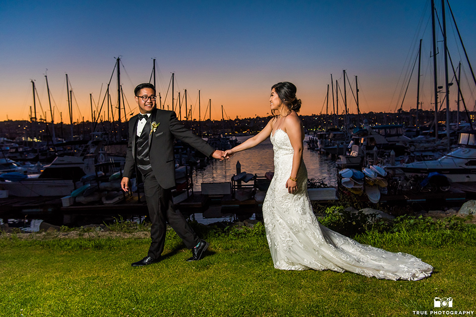  bride in a white lace form fitting gown with a strapless sweetheart neckline, the groom in a black tuxedo with a black bow tie, outside venue