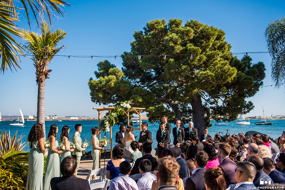  bride in a white lace form fitting gown with a strapless sweetheart neckline, the groom in a black tuxedo with a black bow tie, the groomsmen in black tuxedos with teal bow ties, the the bridesmaids in mint blue gowns and the bridesman in a mint suit to match the girls’ gown