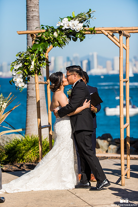  bride in a white lace form fitting gown with a strapless sweetheart neckline, the groom in a black tuxedo with a black bow tie 